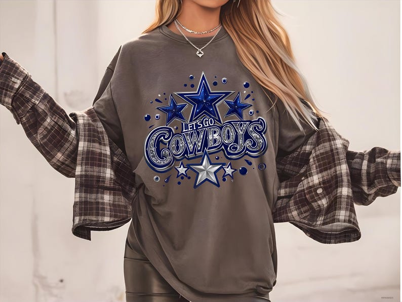 以下が含まれることがあります： グレーのトレーナーに、星と「Let's Go Cowboys」の文字が青と銀で描かれたグラフィックがプリントされています。