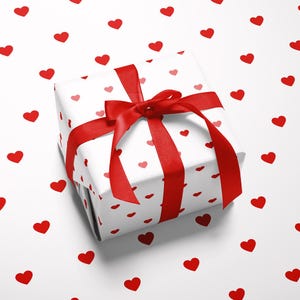 May include: A wrapped gift box with a red ribbon and bow, set against a white background scattered with red heart shapes. The gift wrap features a pattern of small red hearts.