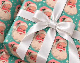 May include: A rectangular gift box wrapped in teal paper featuring a repeating pattern of Santa Claus faces with pink hats and white beards, accented by small white dots and stars. A wide, smooth white satin ribbon is tied in a bow on top.