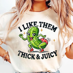 May include: A white t-shirt with a green cartoon pickle wearing red shoes and a red and white polka dot bikini. The text "I like them thick & juicy" is printed on the shirt.