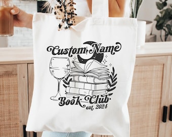 Puede incluir: Bolsa de tela blanca con texto y gráfico negros. El texto dice "Custom Name Book Club est. 2024". El gráfico presenta una copa de vino, una pila de libros, una luna creciente y estrellas.
