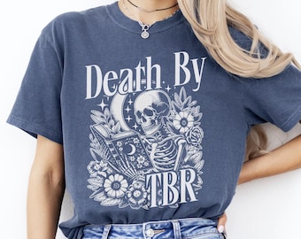 May include: A blue t-shirt with a white graphic of a skeleton holding a book and a skull with the text "Death By TBR".