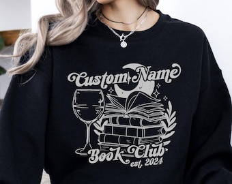 May include: Black sweatshirt with a white graphic design of a wine glass, a stack of books, a crescent moon, and the text "Custom Name Book Club est. 2024".