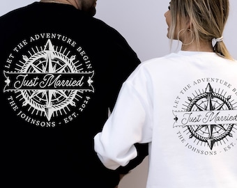 May include: Black and white sweatshirts featuring a compass design. The text on the back says "Let the Adventure Begin" above "Just Married", the couple's surname, and the year 2024. One sweatshirt is black, the other is white.