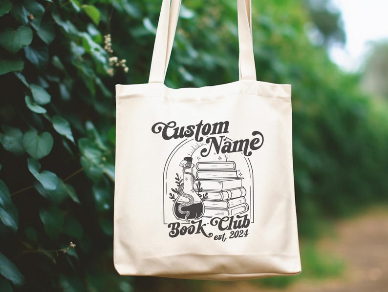 Puede incluir: Una bolsa de tela blanca con texto negro y un gr&aacute;fico. El texto dice "Custom Name Book Club est. 2024". El gr&aacute;fico es una ilustraci&oacute;n en blanco y negro de una pila de libros con una botella de poci&oacute;n y enredaderas.