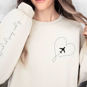 May include: A cream-colored sweatshirt with a black airplane flying through a heart shape on the front. The left sleeve has the text "If you want to go, you will find a way" written in cursive.