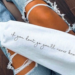 May include: A white sweatshirt with the text "if you don't go you'll never know" written in black cursive script.