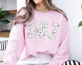 May include: Pink sweatshirt with a floral print design that spells out the word "GOLF" in white letters.