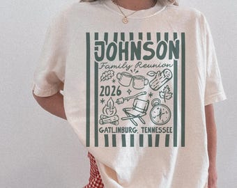 May include: Cream-colored t-shirt with a green graphic design. The design includes the name "JOHNSON Family Reunion 2026" along with camping-themed illustrations and the location "GATLINBURG, TENNESSEE".