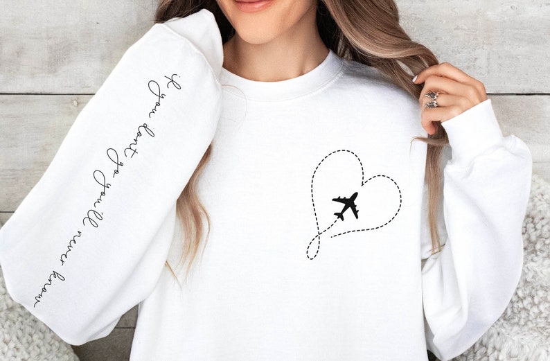 May include: White sweatshirt with a black airplane flying through a dotted line heart on the front. The left sleeve has the text "You will travel far" written in cursive.