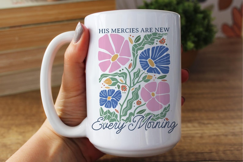 K&ouml;nnte beinhalten: Wei&szlig;er Keramikbecher mit einem Blumendesign in Rosa, Blau und Gr&uuml;n. Der Becher tr&auml;gt den Text "HIS MERCIES ARE NEW Every Morning" in einer dekorativen Schriftart. Der Becher hat einen gro&szlig;en Henkel.