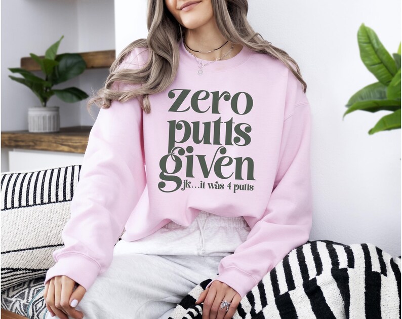 May include: A pink sweatshirt with the text "Zero putts given...jk...it was 4 putts" in black.