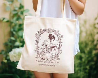 Puede incluir: Una bolsa de tela blanca con una ilustración marrón de una mujer leyendo un libro. La ilustración está rodeada de un diseño floral. El texto "I declare after all, there is no enjoyment like reading" está impreso debajo de la ilustración.