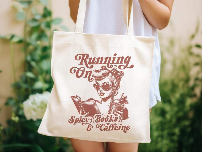 May include: A white canvas tote bag with a red graphic design. The graphic features a woman with red sunglasses reading a book and holding a glass of iced coffee. The text on the bag reads "Running on Spicy Books & Caffeine".