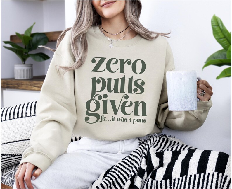 May include: A beige sweatshirt with the text "Zero putts given...jk...it was 4 putts" in dark green letters.