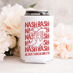 May include: White can cooler with red text and a cowboy boot and hat graphic. The text reads "NASH BASH" multiple times, with "OLIVIA'S BACHLORETTE" at the bottom. The top of the can is visible.