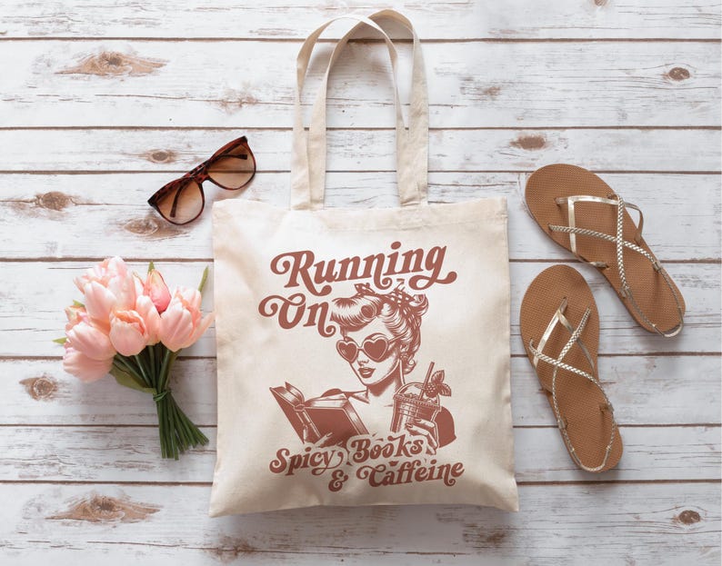 May include: A white tote bag with a brown design featuring a woman with sunglasses and the text "Running on Spicy Books & Caffeine".