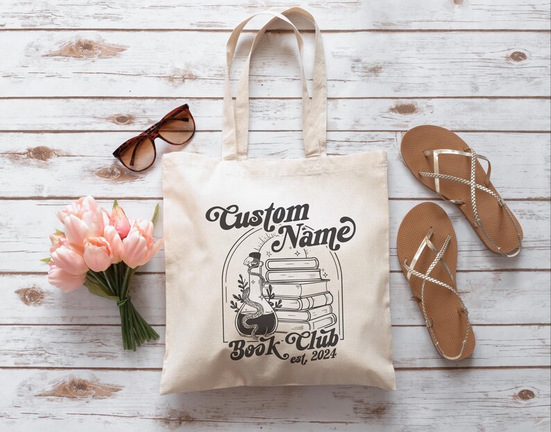 Puede incluir: Una bolsa de tela blanca con texto negro y un gr&aacute;fico de una botella de poci&oacute;n y libros apilados. El texto dice "Custom Name Book Club est. 2024".