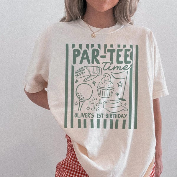 May include: Cream-colored t-shirt with a green and white graphic. The graphic reads "PAR-TEE Time" and features golf-themed illustrations, including a golf ball, glove, and cupcake. The text "OLIVER'S 1ST BIRTHDAY" is also included.
