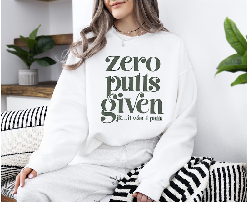 May include: White sweatshirt with the text "zero putts given jk... it was 4 putts" in green.