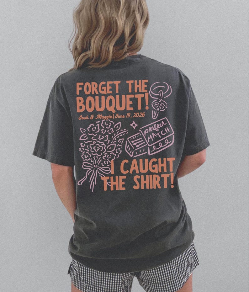 May include: Dark gray t-shirt with the text "FORGET THE BOUQUET!" in orange, along with the names "Josh & Maggie" and the date "June 19, 2026". The shirt also features a bouquet graphic and the phrase "I CAUGHT THE SHIRT!"