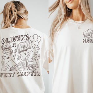 May include: Cream-colored t-shirts with black graphic designs. One shirt features the text "Oliver's First Chapter" with illustrations of books, balloons, and a cupcake. The other shirt has a book design and the word "Mama".