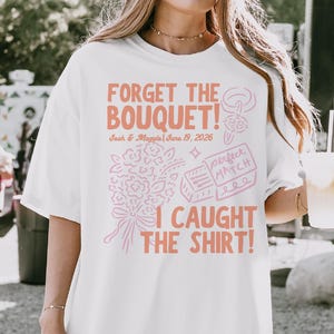 May include: White t-shirt with the text "FORGET THE BOUQUET! I CAUGHT THE SHIRT!" in coral lettering. The shirt also features a bouquet illustration and the names "Josh & Maggie" with the date "June 19, 2026".