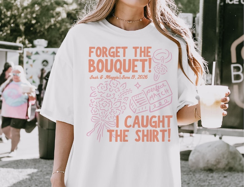 May include: White t-shirt with the text "FORGET THE BOUQUET! I CAUGHT THE SHIRT!" in coral lettering. The shirt also features a bouquet illustration and the names "Josh & Maggie" with the date "June 19, 2026".