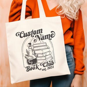 Puede incluir: Bolsa de tela blanca con texto negro y un gr&aacute;fico de una botella de poci&oacute;n con una serpiente y una pila de libros. El texto dice "Custom Name Book Club est. 2024".