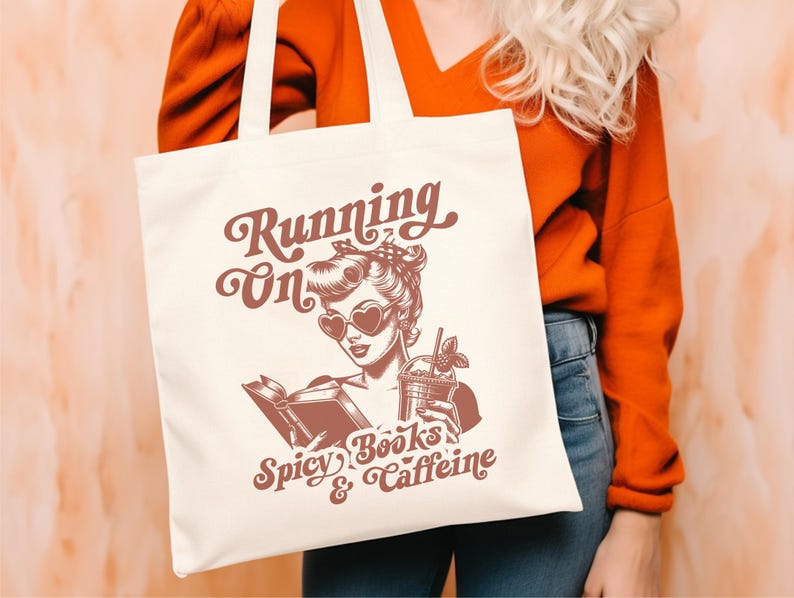 May include: A white tote bag with a red design featuring a woman with a book and a drink. The text on the bag reads "Running on Spicy Books & Caffeine".