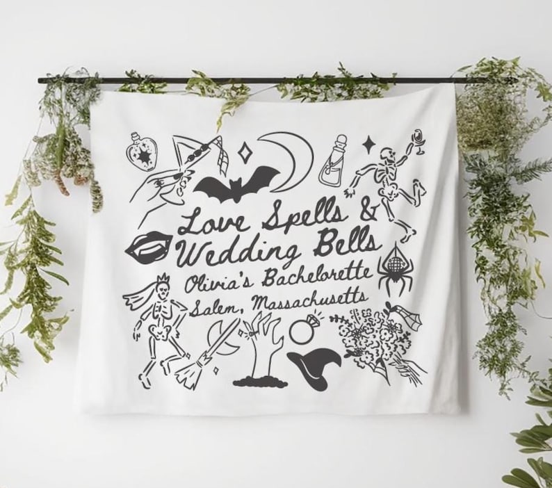 May include: White fabric wall hanging with black illustrations and text. The text reads "Love Spells & Wedding Bells Olivia's Bachelorette Salem, Massachusetts." The design includes a bat, moon, potion bottle, and skeleton.