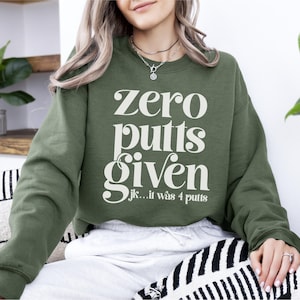 May include: A green sweatshirt with the text "zero putts given...jk...it was 4 putts" in white.