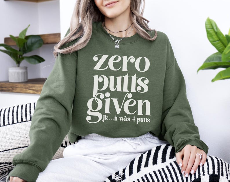 May include: A green sweatshirt with the text "zero putts given...jk...it was 4 putts" in white.