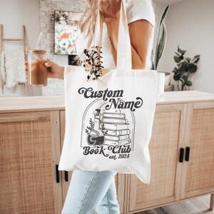Puede incluir: Bolsa de tela blanca con una ilustraci&oacute;n en blanco y negro de una botella de poci&oacute;n y libros apilados. El texto "Custom Name Book Club est. 2024" est&aacute; impreso en la bolsa.