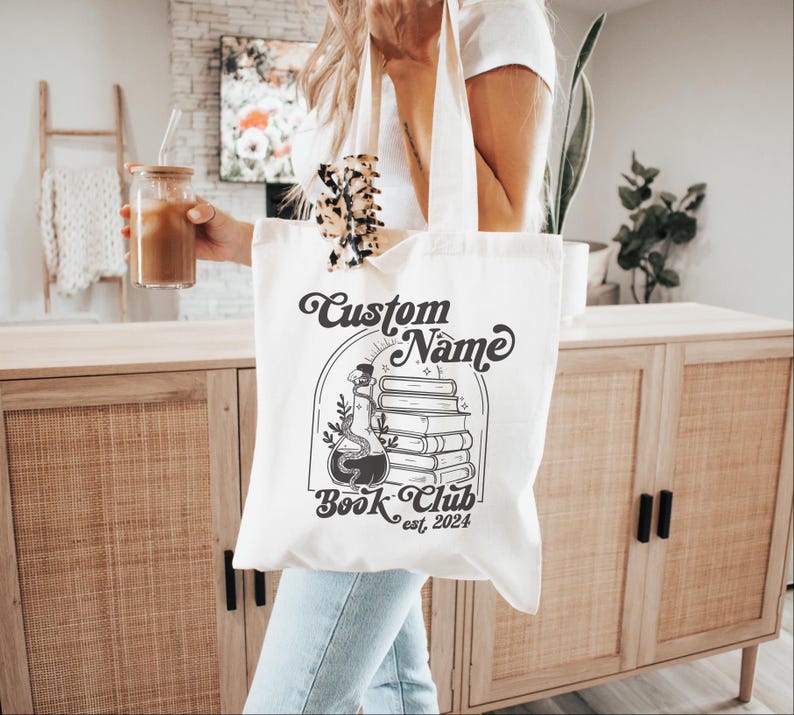 Puede incluir: Bolsa de tela blanca con una ilustraci&oacute;n en blanco y negro de una botella de poci&oacute;n y libros apilados. El texto "Custom Name Book Club est. 2024" est&aacute; impreso en la bolsa.