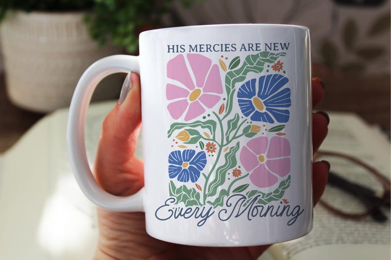 K&ouml;nnte beinhalten: Wei&szlig;e Keramiktasse mit einem Blumendesign in Rosa, Blau und Gr&uuml;n. Die Tasse tr&auml;gt den Text "HIS MERCIES ARE NEW Every Morning" in einer Schreibschrift. Die Tasse hat einen gro&szlig;en, gebogenen Henkel.