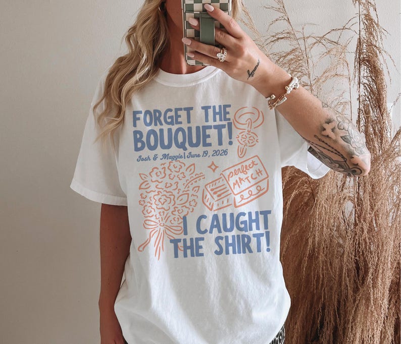 May include: White t-shirt with a blue and peach graphic design. The text reads "FORGET THE BOUQUET!" with the names "Josh & Maggie" and the date "June 19, 2026". Below the text is a bouquet and a matchbox design. The phrase "I CAUGHT THE SHIRT!" is at the bottom.