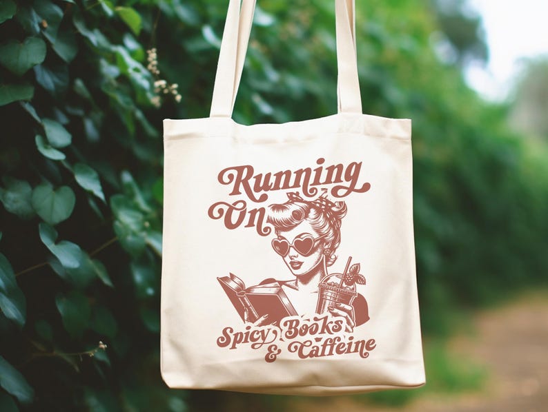 May include: A white tote bag with a red graphic of a woman reading a book and holding a drink. The text on the bag reads "Running on Spicy Books & Caffeine".