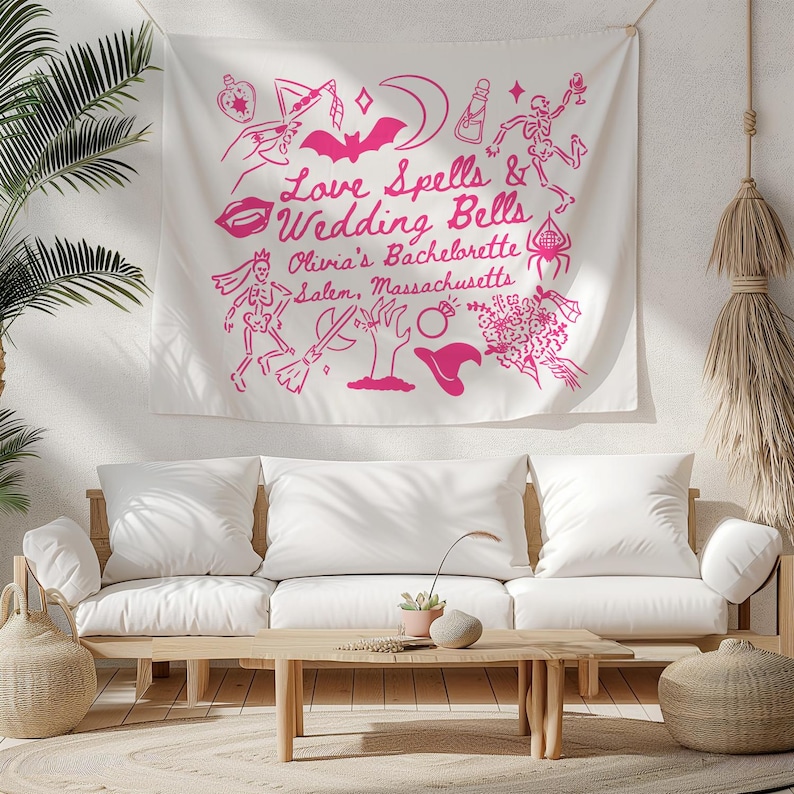 May include: A white tapestry with pink illustrations and text that reads "Love Spells & Wedding Bells Olivia's Bachelorette Salem, Massachusetts." The design includes a bat, moon, skeleton, witch hat, and other themed graphics.