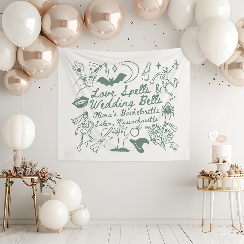 May include: A white fabric banner with green illustrations and text that reads "Love Spells & Wedding Bells, Olivia's Bachelorette, Salem, Massachusetts." The banner is decorated with images of a bat, lips, a witch's hat, and a skeleton. Balloons in white and rose gold are in the background.