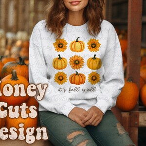 May include: White sweatshirt with a graphic design of pumpkins and sunflowers. The text "it's fall y'all" is printed on the sweatshirt.