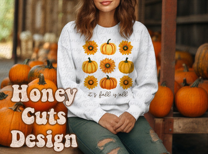 May include: White sweatshirt with a graphic design of pumpkins and sunflowers. The text "it's fall y'all" is printed on the sweatshirt.
