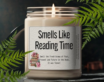 May include: A lit candle in a glass jar with a label that reads "Smells Like Reading Time." The label also features text about the aroma of the past, present, and future. Ferns frame the candle.
