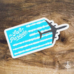 Puede incluir: Una pegatina con la silueta de un avión negro sobre un fondo azul con rayas blancas en forma de nube. El texto "The Soft Parade" está escrito en blanco en el lado izquierdo.