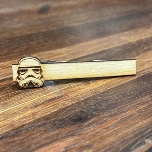 May include: A wooden tie clip featuring a laser-engraved image of a Stormtrooper helmet from Star Wars.