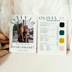 以下が含まれることがあります： 「Olivia Bridesmaid」と黒文字で書かれた白いカードで、背景には2人の女性の画像があります。カードには、日付、場所、ドレス、パーティーに関する情報も記載されています。