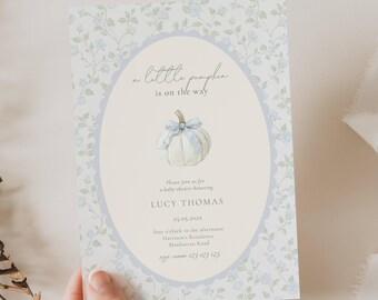 May include: A baby shower invitation with a floral design and the text "a little pumpkin is on the way." The invitation features a watercolor illustration of a pumpkin with a blue bow. The invitation is held by a person.