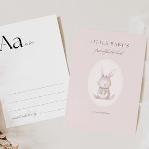 Può includere: Un biglietto rosa con il testo "LITTLE BABY'S first alphabet book" e un'illustrazione ad acquerello di un coniglio marrone con una corona. Il testo "Created with love" è in fondo al biglietto.