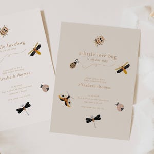 Puede incluir: Dos invitaciones beige para baby shower con ilustraciones de insectos. El texto dice "a little love bug is on the way" e invita a los invitados a celebrar a Elizabeth Thomas. Los insectos decorativos incluyen mariquitas y libélulas.