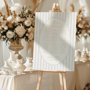 Puede incluir: Un cartel rectangular de plan de asientos para bautizo con rayas verticales azul claro y blancas. El centro muestra un marco ovalado con un icono de paloma, el texto "Please find your seat", nombres de invitados y "Matthew Thomas's BAPTISM".
